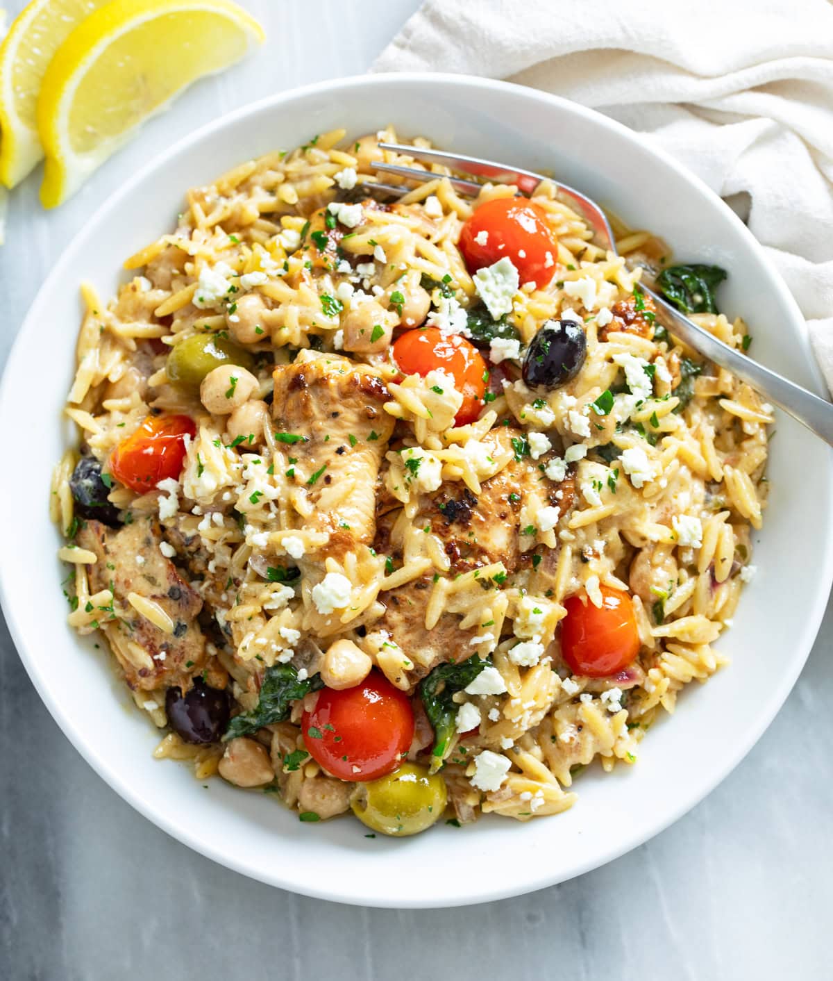 Greek Chicken Orzo in a white bowl with tomatoes, feta, olives, chickpeas, and chicken.