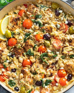 Greek Chicken Orzo in a skillet with olives, tomatoes, spinach, chickpeas, chicken and feta.