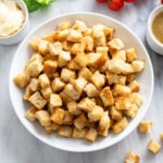 Homemade Croutons in a white bowl with sides of dressing, parmesan, lettuce, and tomatoes.