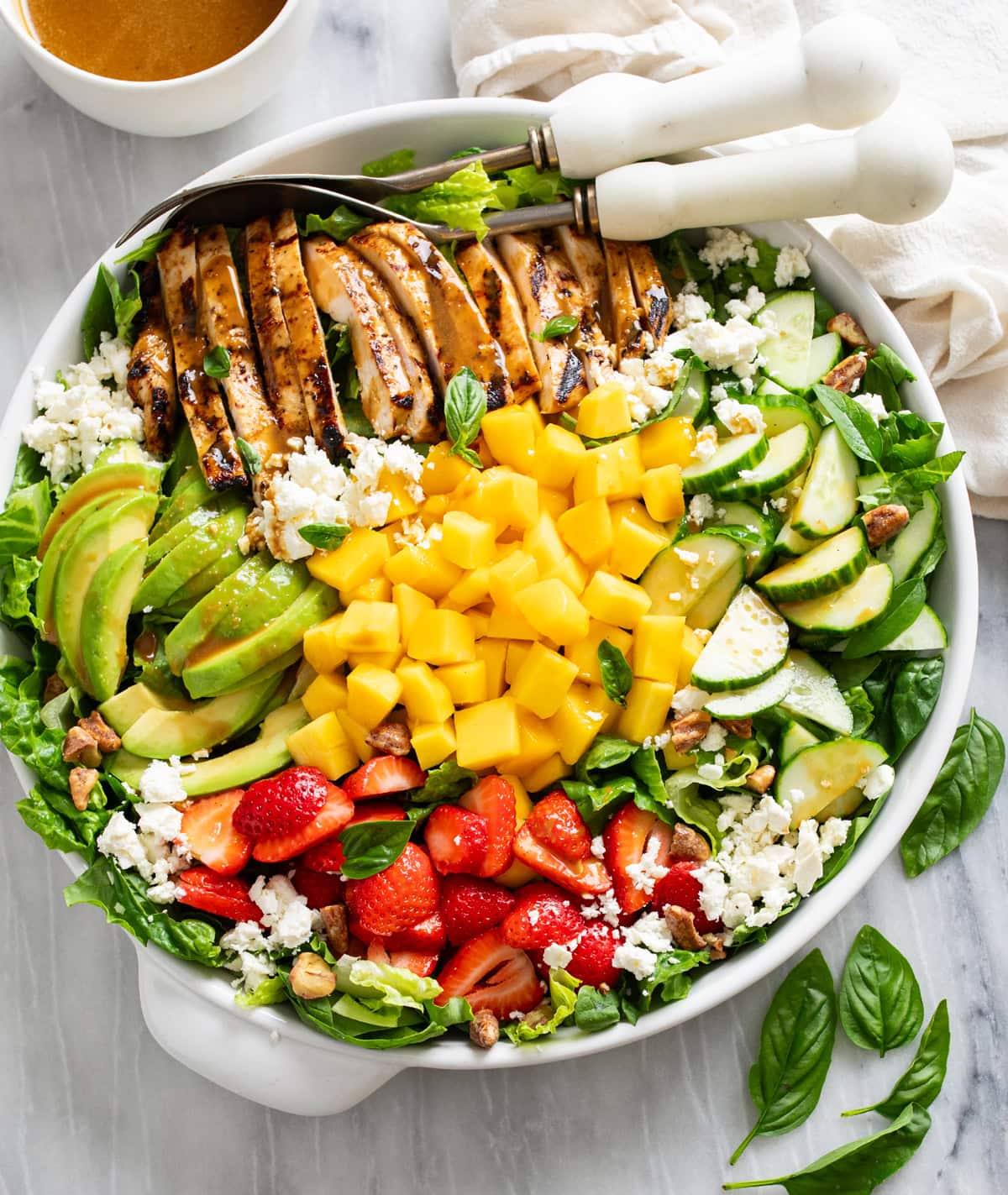 Mango Salad in a white bowl with chicken, sliced avocado, strawberries, cucumbers, mango, feta, and pecans.