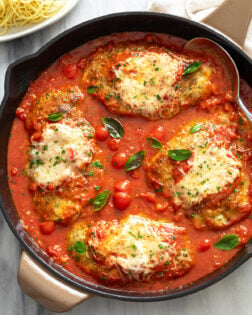 Chicken Pomodoro in a black skillet with fresh tomato sauce, parmesan cheese on top, and fresh basil.