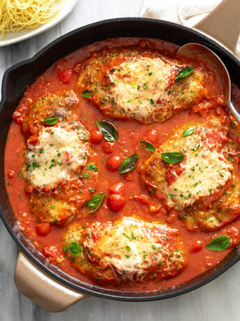 Chicken Pomodoro in a black skillet with fresh tomato sauce, parmesan cheese on top, and fresh basil.