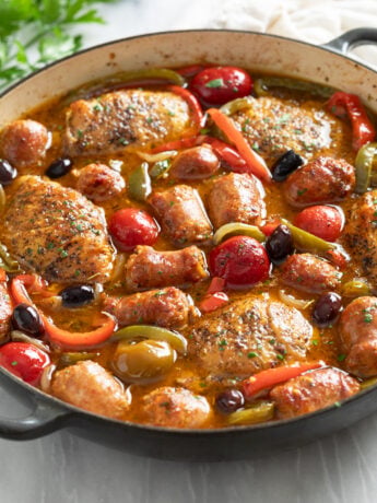 Chicken Scarpariello in a skillet with cherry peppers, bell peppers, and sauce.