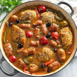 Chicken Scarpariello in a skillet with pan sauce, sausage, chicken thighs, peppers, and cherry peppers.