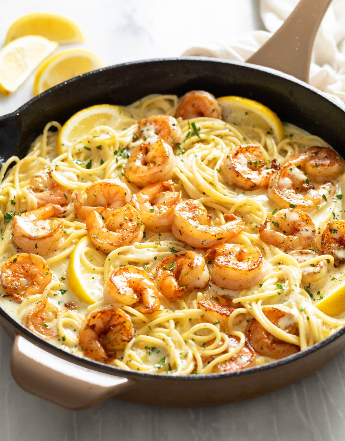 A skillet of Lemon Shrimp Pasta with wedges of lemon, a creamy sauce, and fresh parsley.
