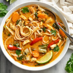 Thai Chicken Soup with noodles, chicken, and vegetables in an orange broth with garnishes.