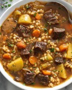 Hearty Beef Barley Soup in a white bowl with fresh parsley on top and a spoon on the side.