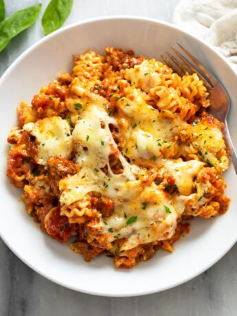 A white bowl filled with Lazy Lasagna with parsley on top and a fork on the side.