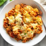Lazy Lasagna in a white bowl with melted mozzarella cheese and parsley on top and a fork on the side.