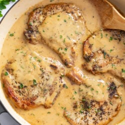 Garlic Parmesan Pork Chops in a skillet with sauce and a wooden spoon on the side.