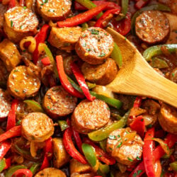 Sausage and Peppers in a skillet with a wooden spoon scooping it up.