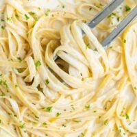 Overhead view of a pan filled with Creamy Fettuccine Alfredo with kitchen tongs.